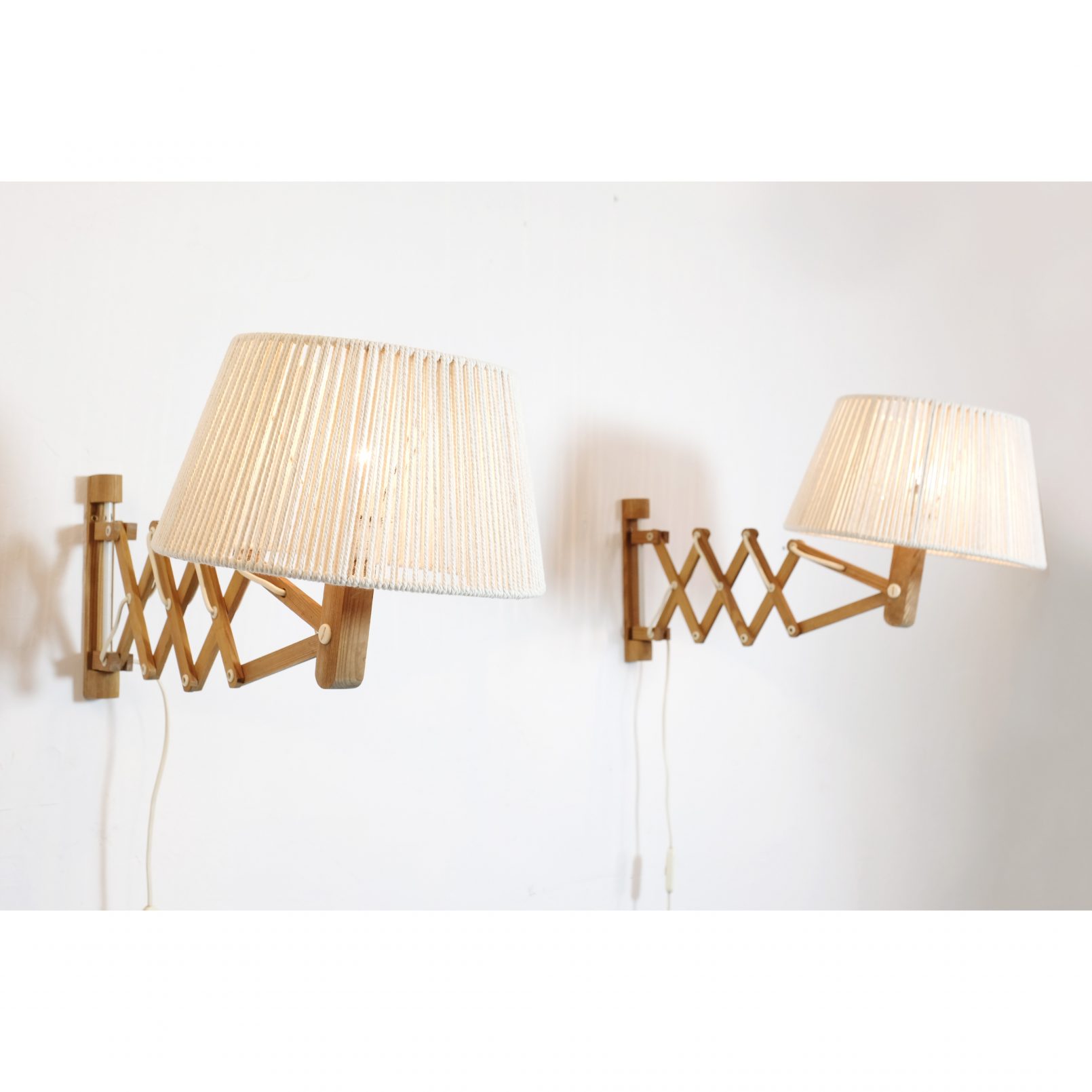 Pair of wooden wall mounted scissor lamps with cotton shades.